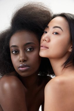 İki güzel genç kadın, Afrikalı ve Asyalı beyaz arka planda iyi korunmuş ciltleri var. Ten renginin çeşitliliği. Çoklu etnik güzellik kavramı, doğal, spa, kozmetoloji, sağlık, reklam.