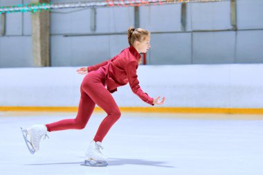 Kırmızı spor giyimli genç kız, buz pateni pistinde buz pateni antrenmanında artistik patinajcı, egzersiz yapıyor. - Sanat. Profesyonel spor kavramı, rekabet, spor okulu, sağlık, hobi, reklam