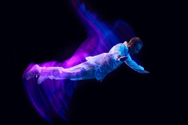 Özgürlük için. Şık giyinmiş genç adam neon ışıklı siyah stüdyo arka planına doğru düşüyor. Havalanma. Hareket kavramı, sanat, dans ve spor, moda, gençlik, reklam