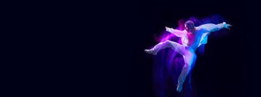 Beyaz giyimli, kaslı genç adam siyah stüdyo arka planında karışık ışık efektiyle zıplıyor. Hareket kavramı, sanat, dans ve spor, moda, gençlik. Pankart. İlan için alanı kopyala