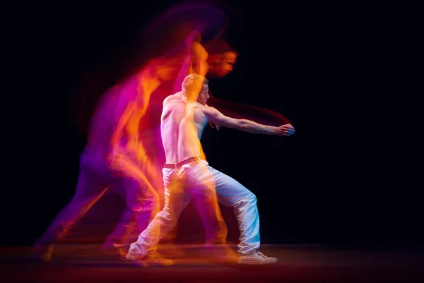 Inner fight. Muscular, shirtless, young guy in motion against black studio background in neon with mixed lights effect. Concept of movements, art, dance and sport, fashion, youth, ad