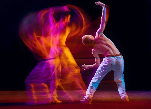 Inspiration and freedom. Young shirtless guy making chaotic movements against black studio background in neon with mixed lights effect. Concept of movements, art, dance and sport, fashion, youth, ad