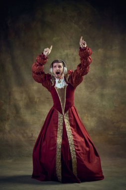 Genç adam, ortaçağ prensi, kadın elbiseli hükümdar kulaklıkla müzik dinleyen, klasik arka planda dans eden. Tarihi retrospektifler, moda, kışkırtıcı projeler, cinsiyet akışkanlığı kavramı