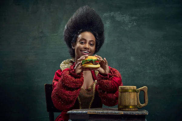 美丽的非洲女人 中世纪的公主吃美味的汉堡与古老的绿色背景 美与时尚的概念 时代的比较 — 图库照片