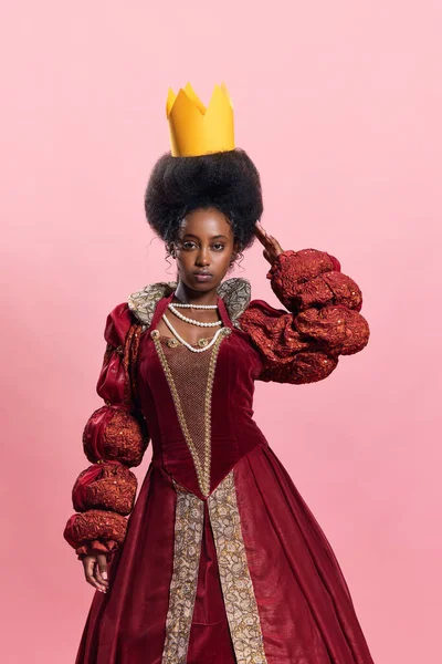 皇家的优雅 年轻非洲女子的肖像 中世纪的公主穿着老式服装 手持纸制王冠 背景为粉色工作室 美与时尚的概念 时代的比较 — 图库照片