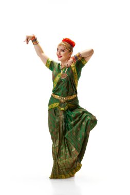 Yeşil elbiseli güzel bir kadın beyaz stüdyo arka planında geleneksel Hint dansı bharatanatyam dansı yapıyor. Güzellik, moda, Hindistan, gelenekler, yaşam tarzı, koreografi, sanat. Ad