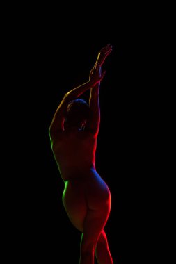 Neon ışıklarıyla siyah stüdyo arka planında poz veren hassas, şehvetli, çıplak bir kadın. Kadın güzelliği, vücut sanatı, estetik, kadınlık ve duygusallık kavramı..