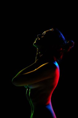 Şefkat ve duygusallık. Seksi, güzel bir kadın, neon ışıklarıyla siyah stüdyonun arka planında çıplak poz veriyor. Kadın güzelliği, vücut sanatı, estetik, kadınlık ve duygusallık kavramı..