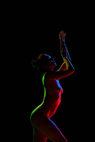 Freedom and acceptance. Slim, tender woman posing naked against black studio background in neon lights. Concept of female beauty, body art, aesthetics, femininity and sensuality.
