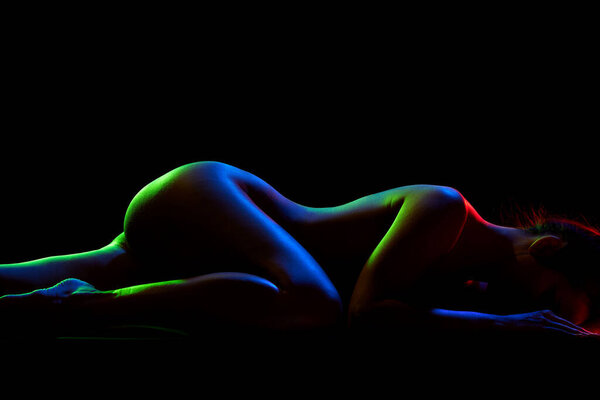 Cropped image of tender, sensual female body lying on floor against black studio background in neon lights. Concept of female beauty, body art, aesthetics, femininity and sensuality. Copy space for ad