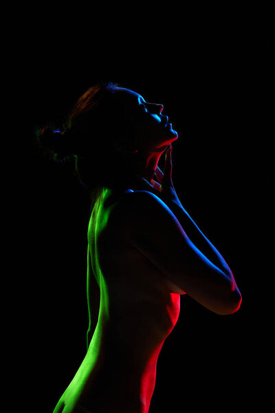Tenderness and sensuality. Sexy, beautiful woman posing naked against black studio background in neon lights. Concept of female beauty, body art, aesthetics, femininity and sensuality.