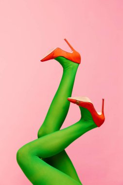 Renkler uyuşuyor. Yeşil taytlı ince kadın bacakları ve pembe arka planda turuncu topuklu ayakkabılar. Renkli fotoğrafçılık. Moda anlayışı, yaratıcılık, hayal gücü. İlan için alanı kopyala