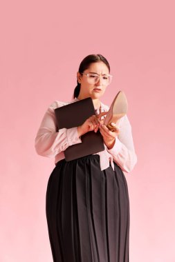 Bluz ve etekli kadın çıplak ayakla ayakta duruyor, topuklu ayakkabıları pembe arka planda cep telefonu gibi kullanıyor. Ölüler. İş anlayışı, güzellik, insan duyguları, yaşam tarzı, moda, reklam