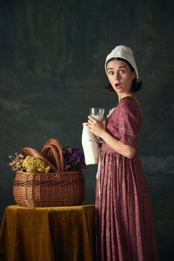 Şok edici ve beklenmedik bir buluşma. Duygusal genç kadın, koyu renkli arka plana karşı sütle ayakta duran ortaçağ hizmetçisi. Tarih kavramı, çağların karşılaştırması, güzellik, sanat, yaratıcılık