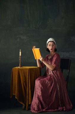 Romantik romanlar. Masada oturan ve klasik yeşil arka plana karşı kitap okuyan Rönesans hizmetçisi imajındaki zarif genç kadın. Tarih kavramı, çağların karşılaştırması, güzellik, sanat, yaratıcılık