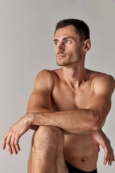 一个有着灰色眼睛的英俊年轻男子的画像 在灰色的工作室背景下 他的造型是赤裸的 肌肉的身体 男人的健康与美的概念 身体护理 — 图库照片