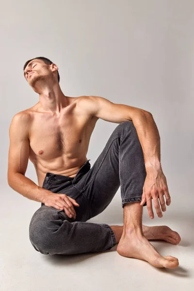 Man with muscular, strong, relief body posing shirtless in jeans against grey studio background. Well-being. Concept of mens health and beauty, body care, fitness, wellness, ad