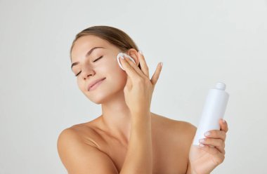 Beyaz arka planda izole edilmiş yüz toneri kullanan iyi korunmuş, pürüzsüz derisi olan güzel genç bir kadın. Doğal güzellik kavramı, kozmetik ve kozmetik, cilt bakımı, kaplıca. Ad