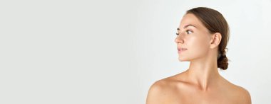 Beyaz arka planda çıplak omuzlu güzel bir genç kadının portresi. Yumuşak, bakımlı bir ten. Doğal güzellik kavramı, kozmetik ve kozmetik, cilt bakımı, kaplıca. Reklam. Pankart