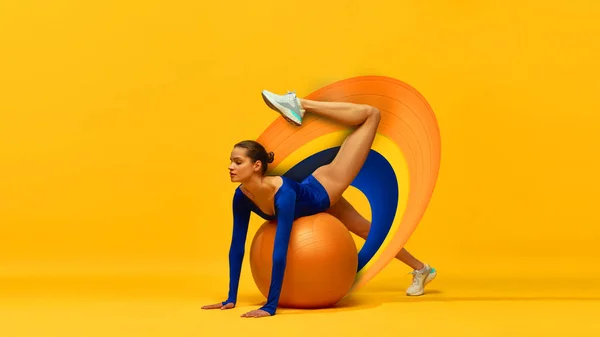 Stretching. Beautiful young girl in blue bodysuit training with fitness ball onyellow background with abstract design element. Contemporary art collage. Concept of sport, action and motion, health