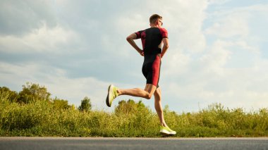 Spor giyimli rekabetçi bir adamın dinamik görüntüsü, atlet yaz günü açık havada antrenman yapıyor, koşuyor. Maraton. Profesyonel spor anlayışı, triatlon hazırlığı, rekabet, atletizm