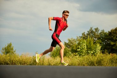 Spor giyimli rekabetçi bir adamın dinamik görüntüsü, atlet yaz günü açık havada antrenman yapıyor, koşuyor. Maraton. Profesyonel spor anlayışı, triatlon hazırlığı, rekabet, atletizm