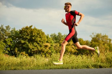 Spor giyimli rekabetçi bir adamın dinamik görüntüsü, atlet yaz günü açık havada antrenman yapıyor, koşuyor. Maraton. Profesyonel spor anlayışı, triatlon hazırlığı, rekabet, atletizm