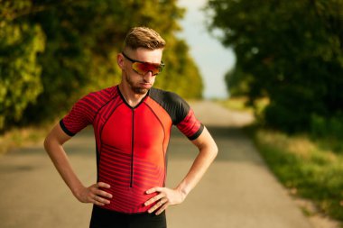 Yorgun hissediyorum. Spor giyimli sporcu sıkı antrenmandan ve dinlenmeden sonra ayakta duruyor. Profesyonel spor anlayışı, triatlon hazırlığı, rekabet, atletizm