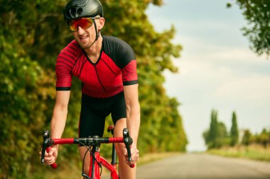Profesyonel triatlet dışarıda antrenman yapıyor, spor giyim ve kask giyiyor, yol boyunca bisiklet sürüyor. Profesyonel spor anlayışı, triatlon hazırlığı, rekabet, atletizm