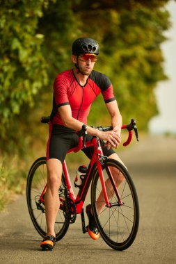 Profesyonel triatlet dışarıda antrenman yapıyor, spor giyim ve kask giyiyor, yol boyunca bisiklet sürüyor. Profesyonel spor anlayışı, triatlon hazırlığı, rekabet, atletizm