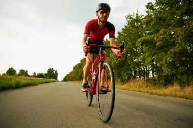 Motive olmuş sporcunun dinamik görüntüsü, yol boyunca bisiklet süren sporcu, açık havada antrenman yapan. Profesyonel spor anlayışı, triatlon hazırlığı, rekabet, atletizm