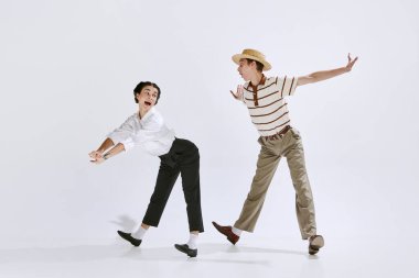 Beautiful young woman and man in stylish retro clothes dancing lindy hop isolated on white studio background. Vintage. Concept of art, hobby, retro dance style, choreography, beauty. Ad clipart