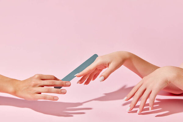 Female hand with nail file taking care after hands, nails against pink background. Elegant natural look. Concept of hand care, cosmetics and cosmetology, spa, natural beauty. Poster, ad