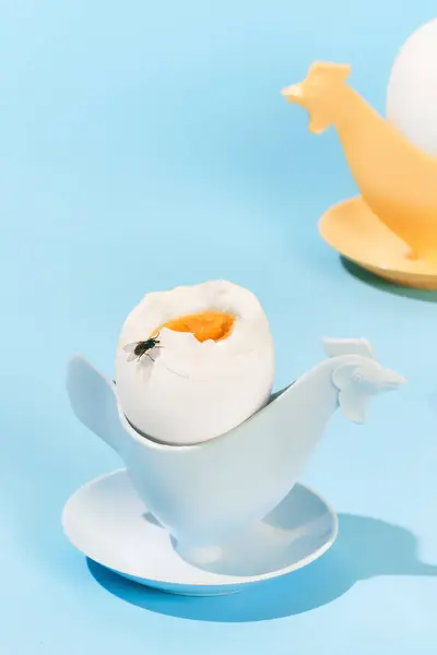 Soft boiled eggs in egg cup over light blue background. Fly sitting on delicious egg. Concept of breakfast, food, taste, health, creativity. Pop art photography. Poster. Copy space for ad