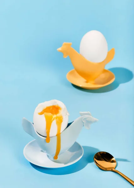 Soft boiled egg with liquid yolk in egg cup with golden spoon over light blue background. Concept of breakfast, food, taste, health, creativity. Pop art photography. Poster. Copy space for ad