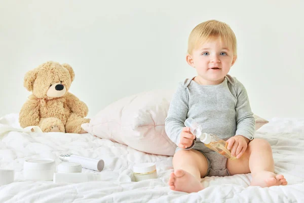 かわいい 小さな赤ん坊の女の子は 自宅でベッドに座って ボディローションを保持しています ボディとスキンケア 保湿プロダクト 子供時代のコンセプト キッズコスメ 自然化粧品 ボディケア — ストック写真