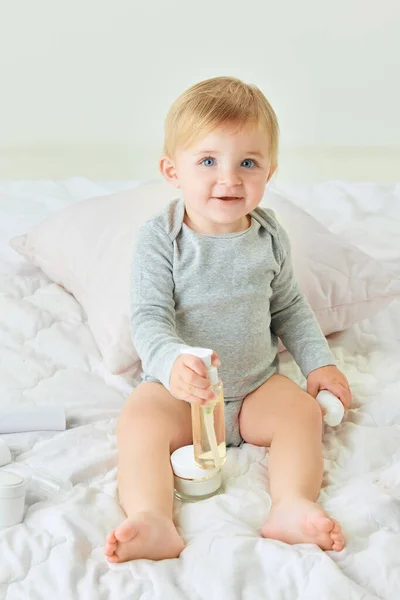 かわいい 美しい 小さな赤ちゃんの女の子は ベッドに座って クリームを保持し ボディ保湿クリーム ボディケア製品 子供時代のコンセプト キッズコスメ 自然化粧品 — ストック写真