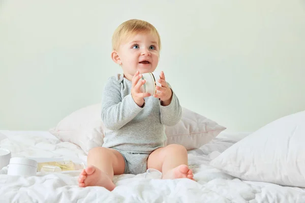 美しい少女 ベッドに座っている青い目を持つ幼児 保湿クリームを保持します スキンケア 子供時代のコンセプト キッズコスメ 自然化粧品 ボディケア — ストック写真