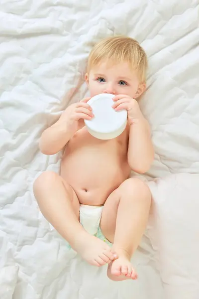 かわいい 美しい子供 ベッドに横たわる小さな女の子 保湿クリームを持っています スキンケア 皮膚科治療 子供時代のコンセプト キッズコスメ 自然化粧品 ボディケア — ストック写真