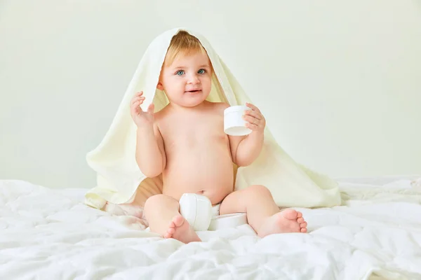 シャワーボディケアの後 タオルと保湿クリームでベッドに座っている小さな女の子 子供時代のコンセプト キッズコスメ 自然化粧品 ボディケア — ストック写真