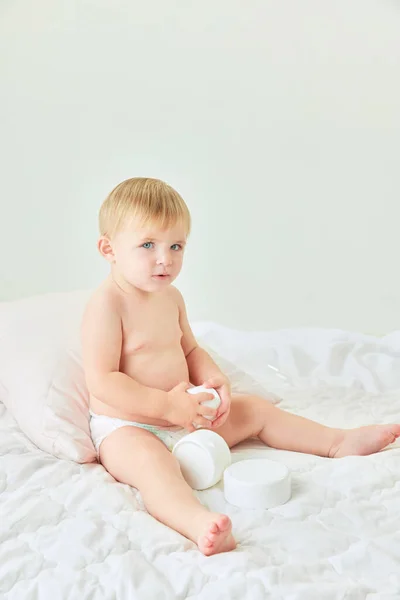美しい かわいい小さな女の子 トッドラーはスキンケア製品でベッドに座っています クリームで保湿ボディ 子供時代のコンセプト キッズコスメ 自然化粧品 ボディケア — ストック写真