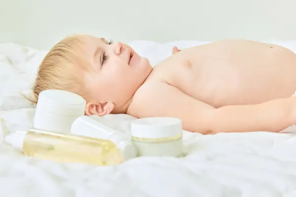 幸せな 素敵な子供 スキンケア製品で自宅でベッドに横たわっている小さな女の子 クリームで保湿ボディ 子供時代のコンセプト キッズコスメ 自然化粧品 ボディケア — ストック写真
