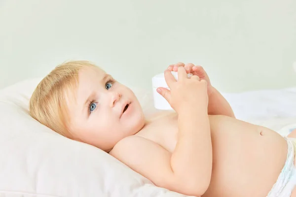 かわいい幼児 小さな赤ん坊の少女 ベッドに横たわって保湿ボディクリームを保持している青い目を持つ子供 ホームケア 子供時代のコンセプト キッズコスメ 自然化粧品 ボディケア — ストック写真