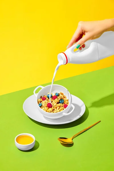朝のバイブ 女性の手は 甘いミューズリとボウルにミルクを注ぐ 緑の黄色の背景に対する果実とシリアル 健康的な食べ物 ポップアート 味の概念 ポスター Adのためのスペースをコピーする — ストック写真