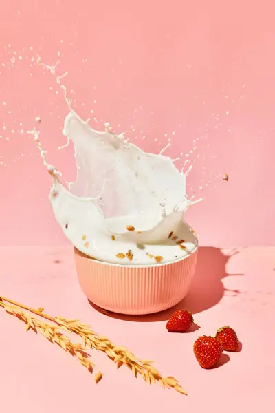 Bowl with splashing milk, cereal, muesli and berries against pink background. Healthy breakfast. Concept of healthy food, nutrition, pop art style, taste. Poster. Copy space for ad