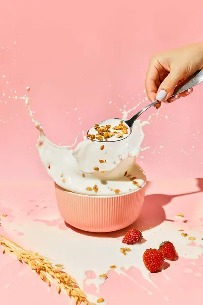 Bowl with splashing milk and female hand putting muesli, cereal against pink background. Healthy breakfast. Concept of healthy food, nutrition, pop art style, taste. Poster. Copy space for ad