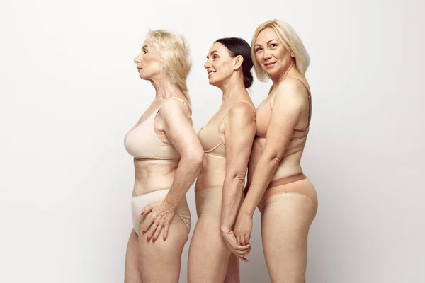Side view image of female bodies in underwear against grey studio background. Natural body of senior women, aging. Concept of age, natural beauty. body and skin care, healthy lifestyle