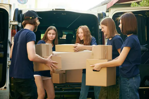 Group of young people, man and women, volunteers loading many boxes of humanitarian goods into van. Concept of humanitarian aid, assistance and support, care, social programs