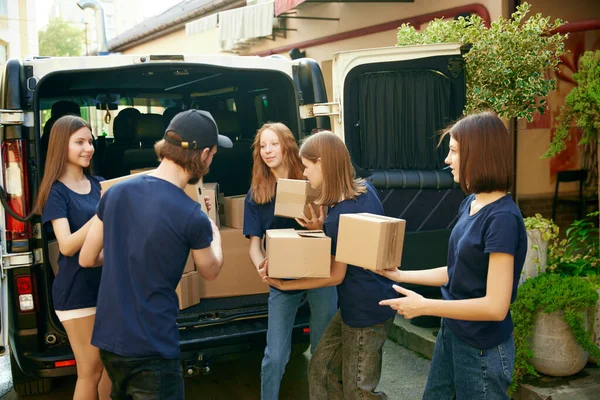 Young people, volunteers in uniform loading boxes into van. Gathering food, clothes, meds for people and animals in need. Concept of humanitarian aid, assistance and support, care, social programs