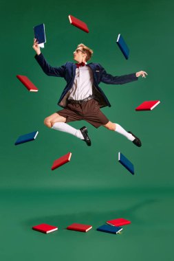 Genç adam, hareketli kitaplar okuyan, atlayan, yeşil stüdyo geçmişine karşı sınavlara hazırlanan bir öğrenci. Ev ödevi. İnsan duyguları, yaşam tarzı, iş ve eğitim kavramı, moda. Ad